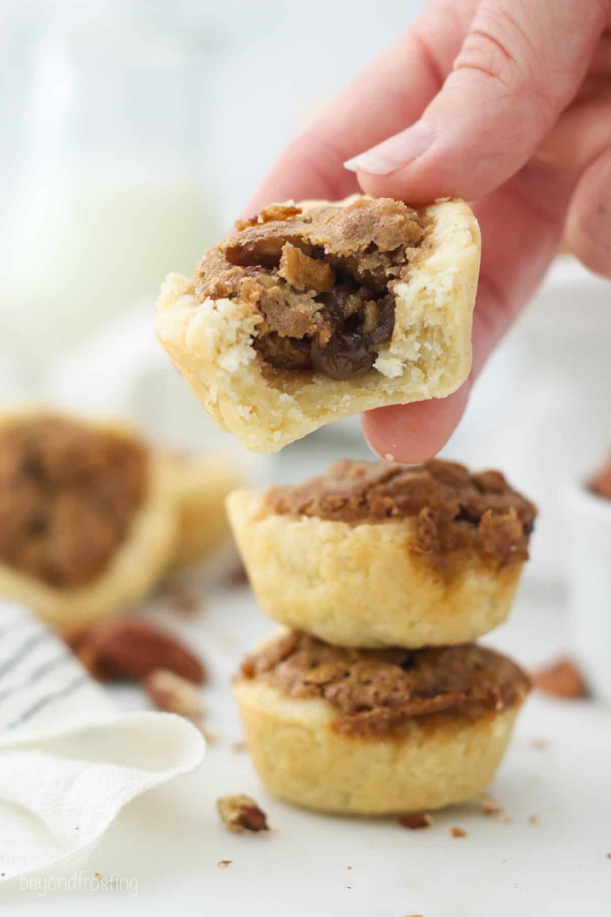 A hand holding a mini pecan tart above two more tarts stacked on top of one another.