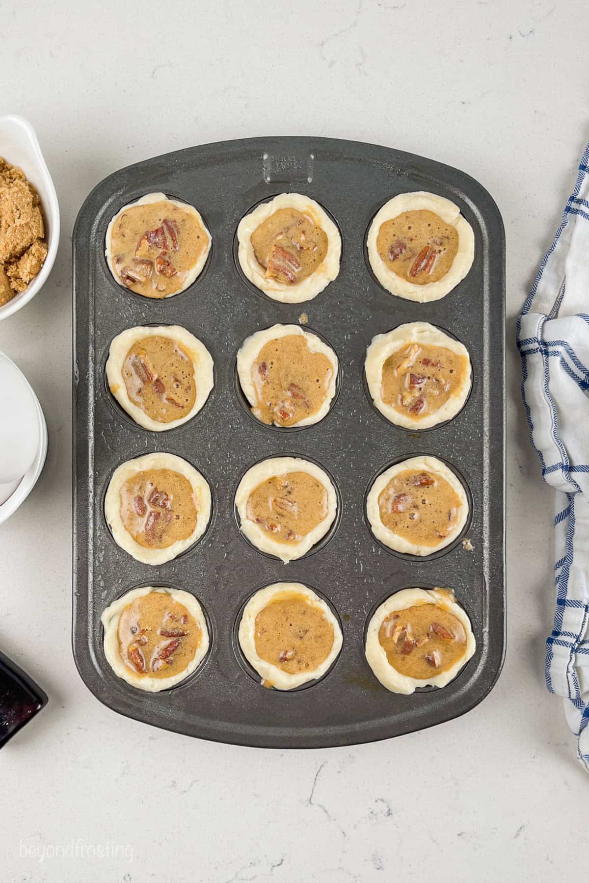 Crusts filled with pecan pie filling in a 12-well mini muffin tin.