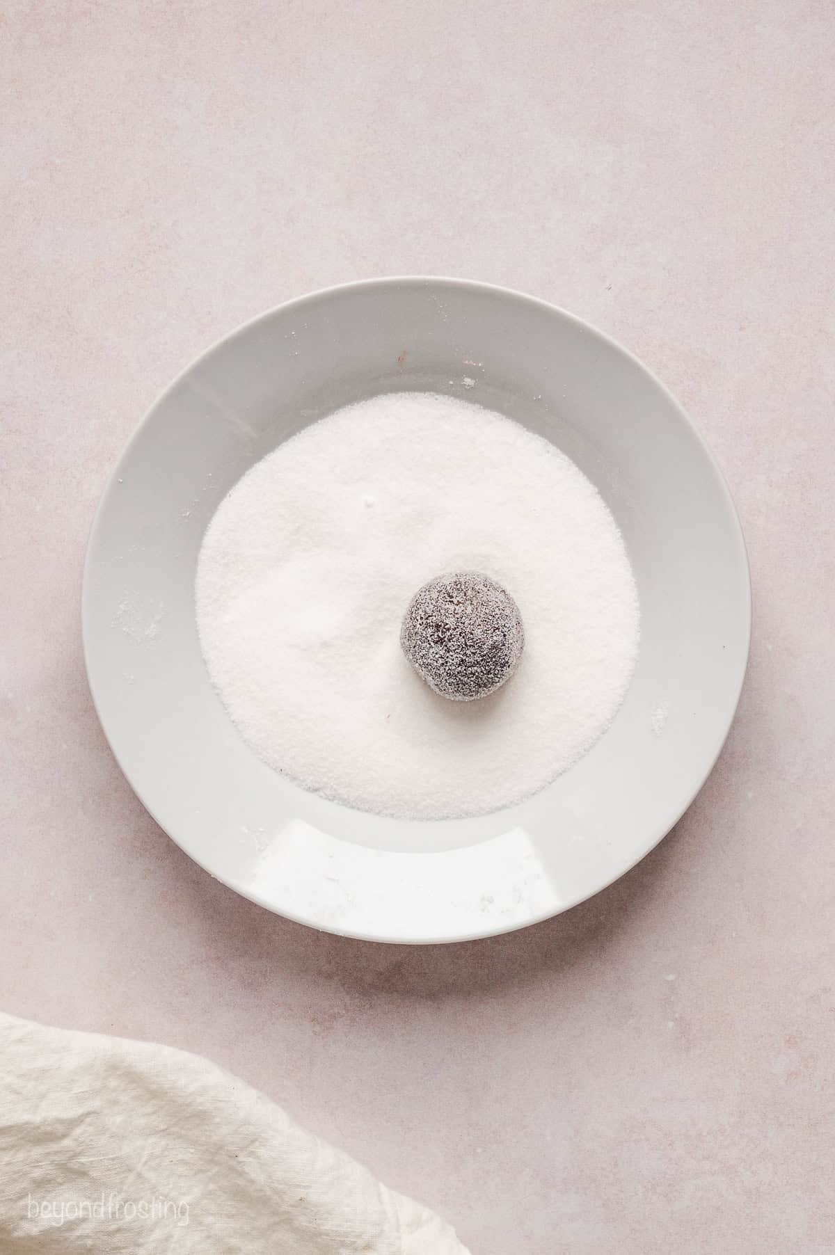 A sugar-coated chocolate cookie dough ball resting in a bowl of granulated sugar.