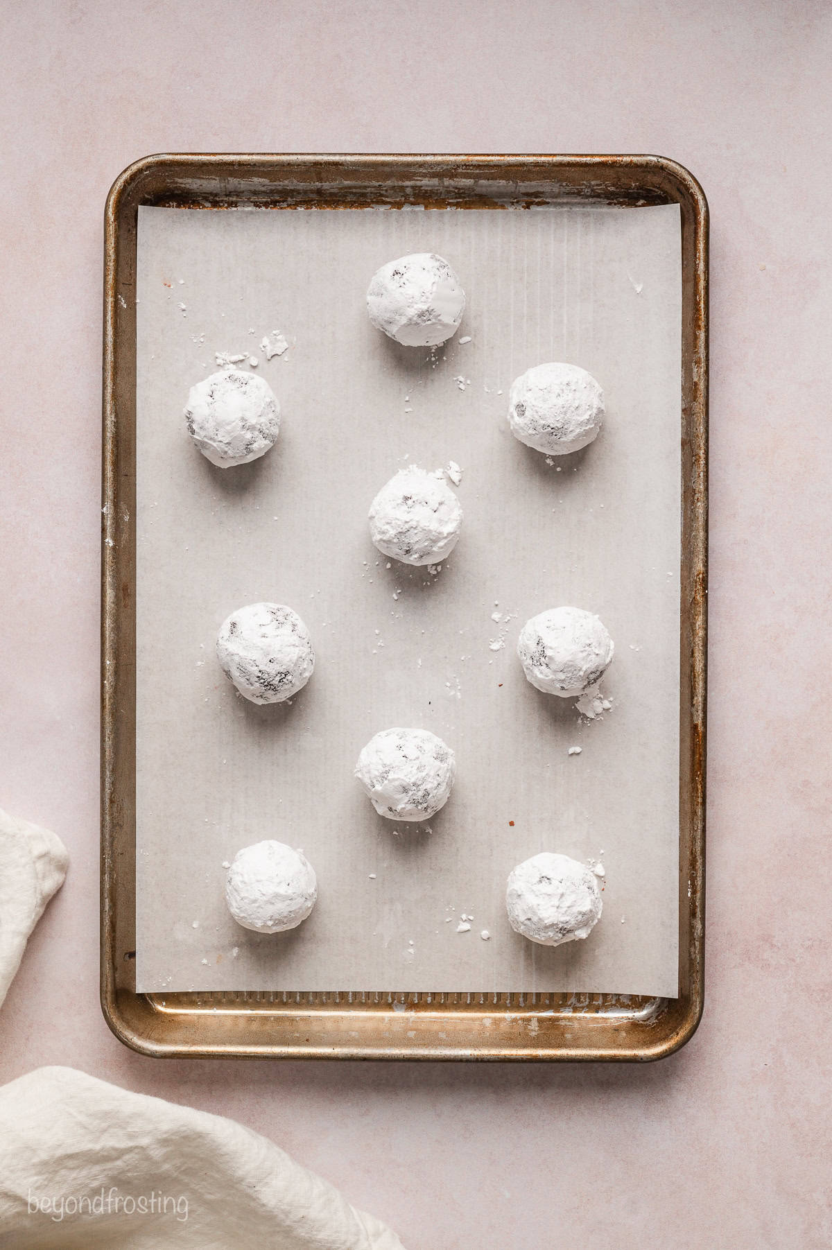 Chocolate cookie dough balls coated with powdered sugar on a parchment-lined baking sheet.