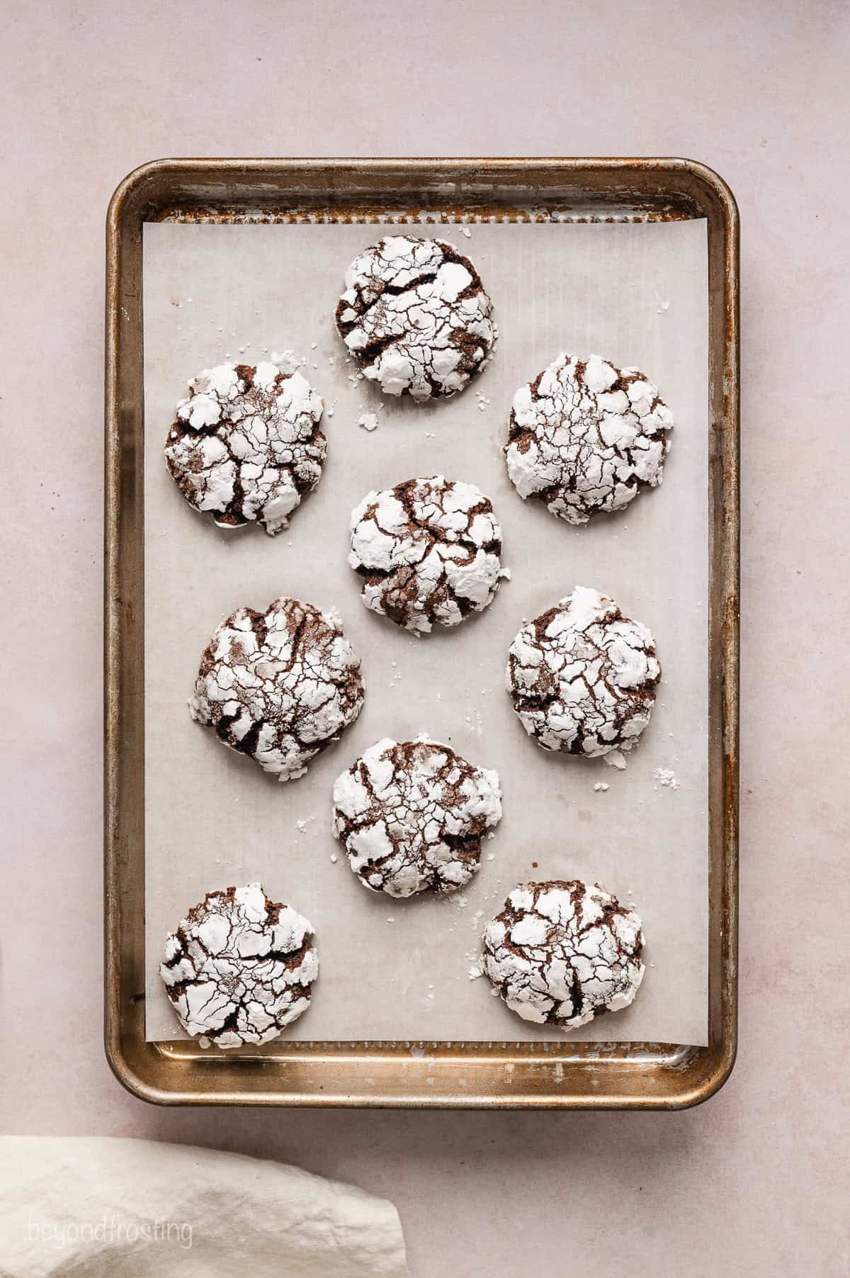 Baked chocolate crinkle cookies dusted with powdered sugar on a parchment-lined baking sheet.