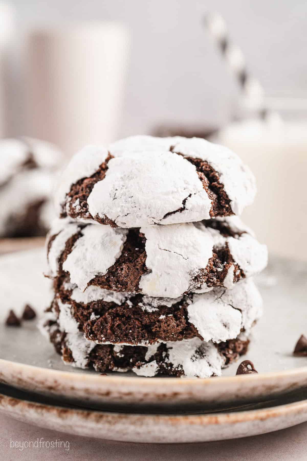 Four chocolate crinkle cookies stacked on a plate.