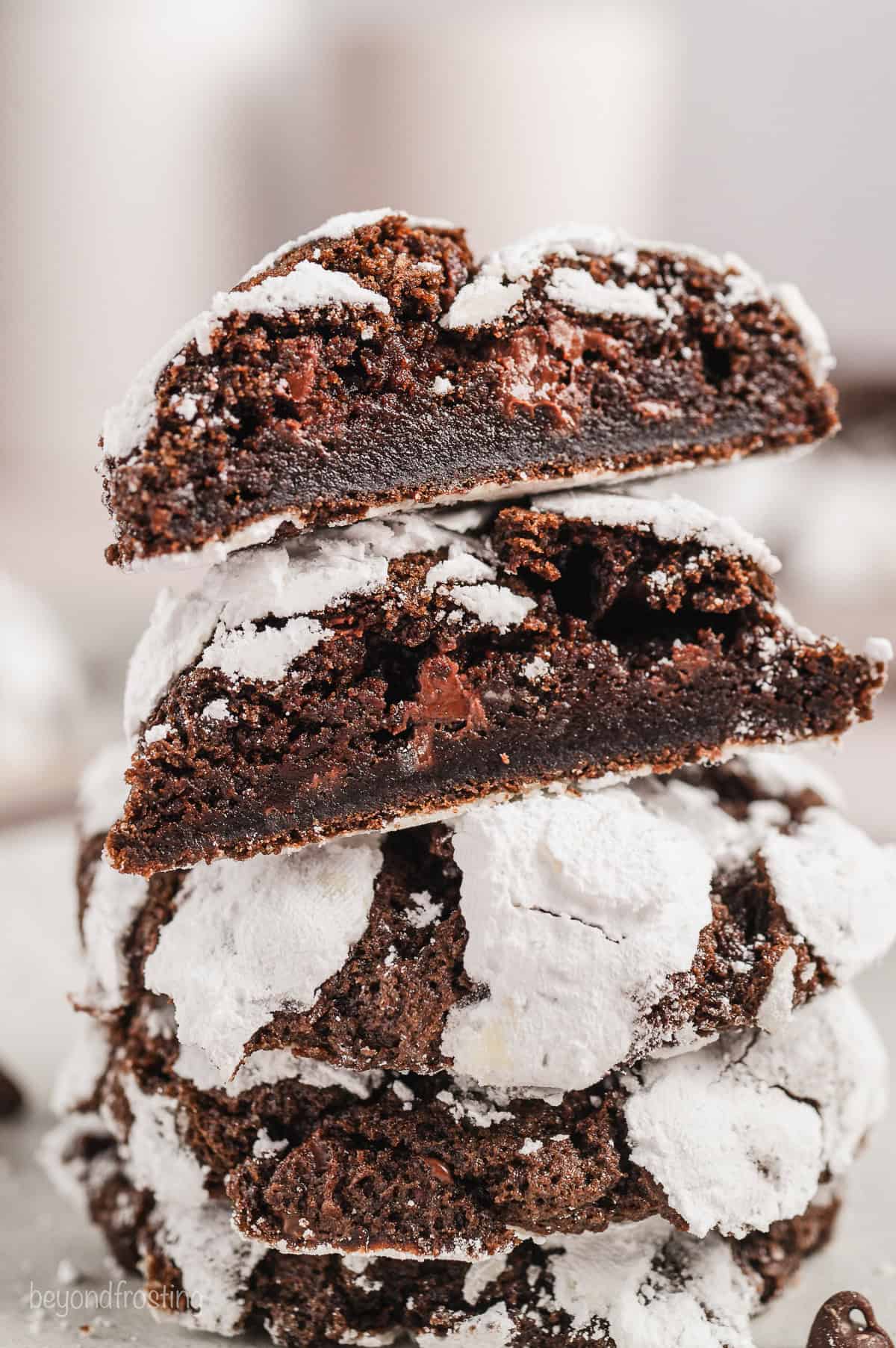 Chocolate crinkle cookies stacked, with the top cookie cut in half to reveal the chocolate chips inside.