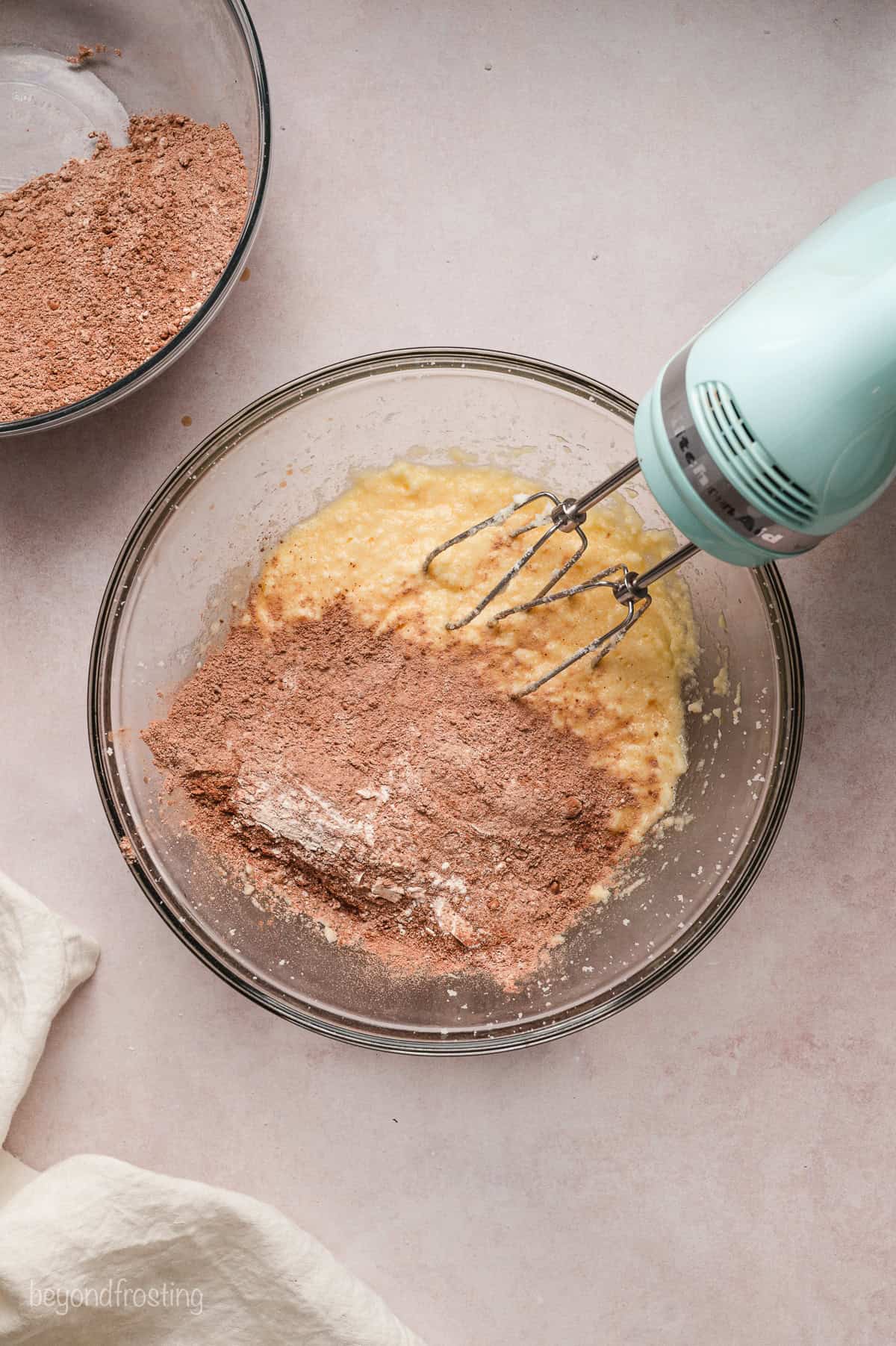 A hand mixer resting in a bowl of cookie dough combined with cocoa powder.