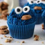 Close up of a Cookie Monster cupcake surrounded by scattered mini Chips Ahoy cookies, with more cupcakes in the background.