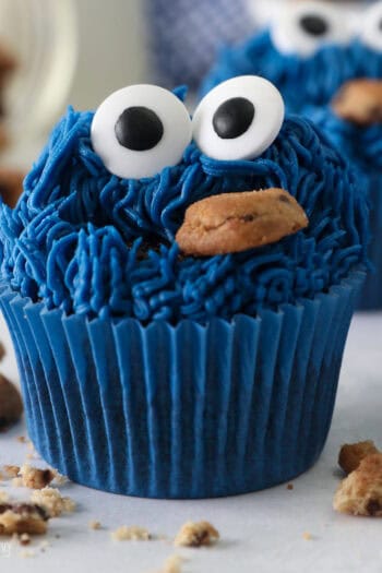 Close up of a Cookie Monster cupcake surrounded by scattered mini Chips Ahoy cookies, with more cupcakes in the background.