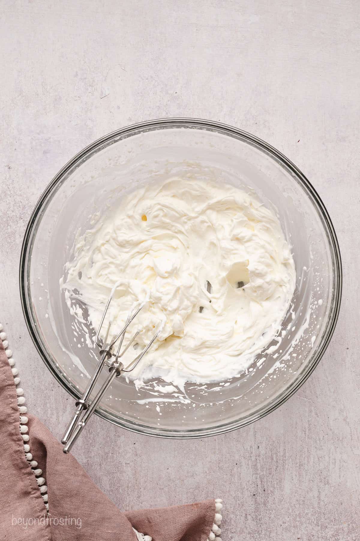 Whipped cream in a glass bowl with a whisk.