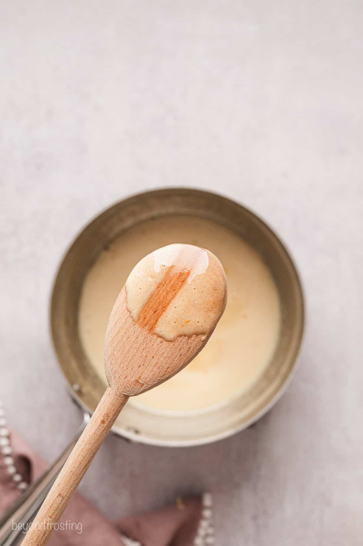 A wooden spoon coated with egg mixture held above a saucepan.