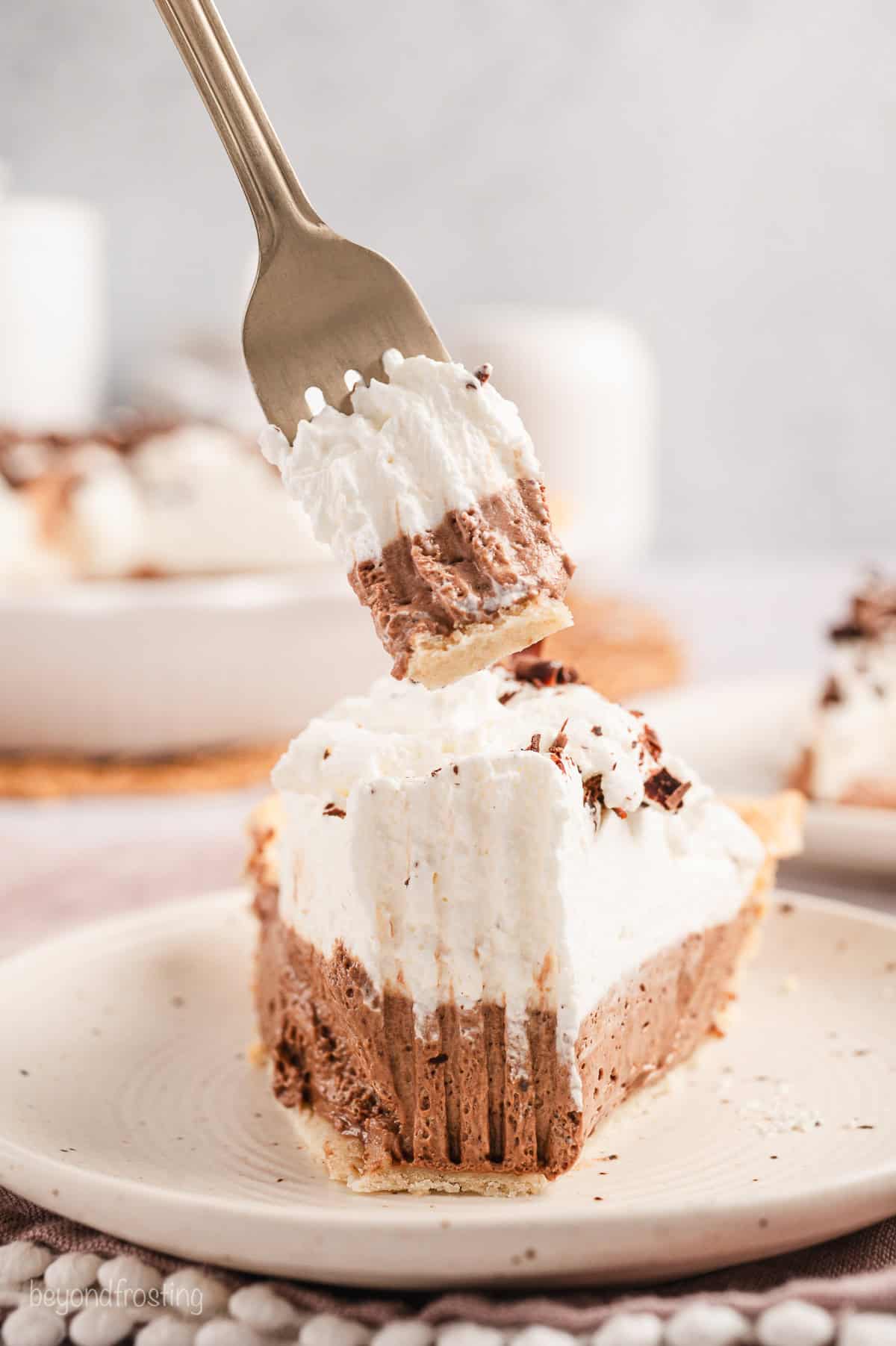 A fork lifting a bite of French silk pie from the end of a slice on a plate.