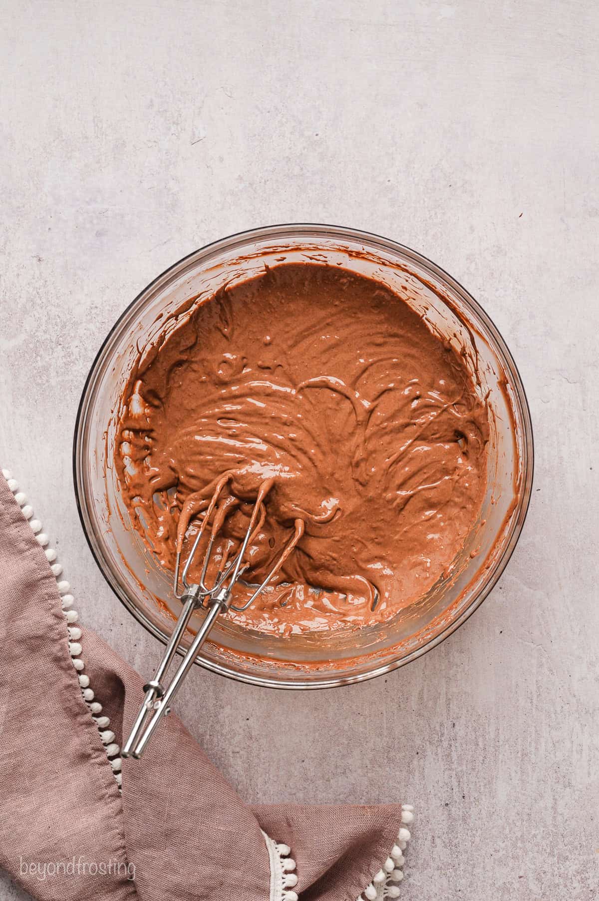 Chocolate pudding in a glass bowl with a whisk.