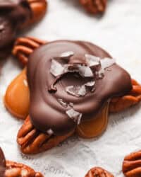 Close up of turtle candies topped with flaky sea salt on a sheet of parchment paper.