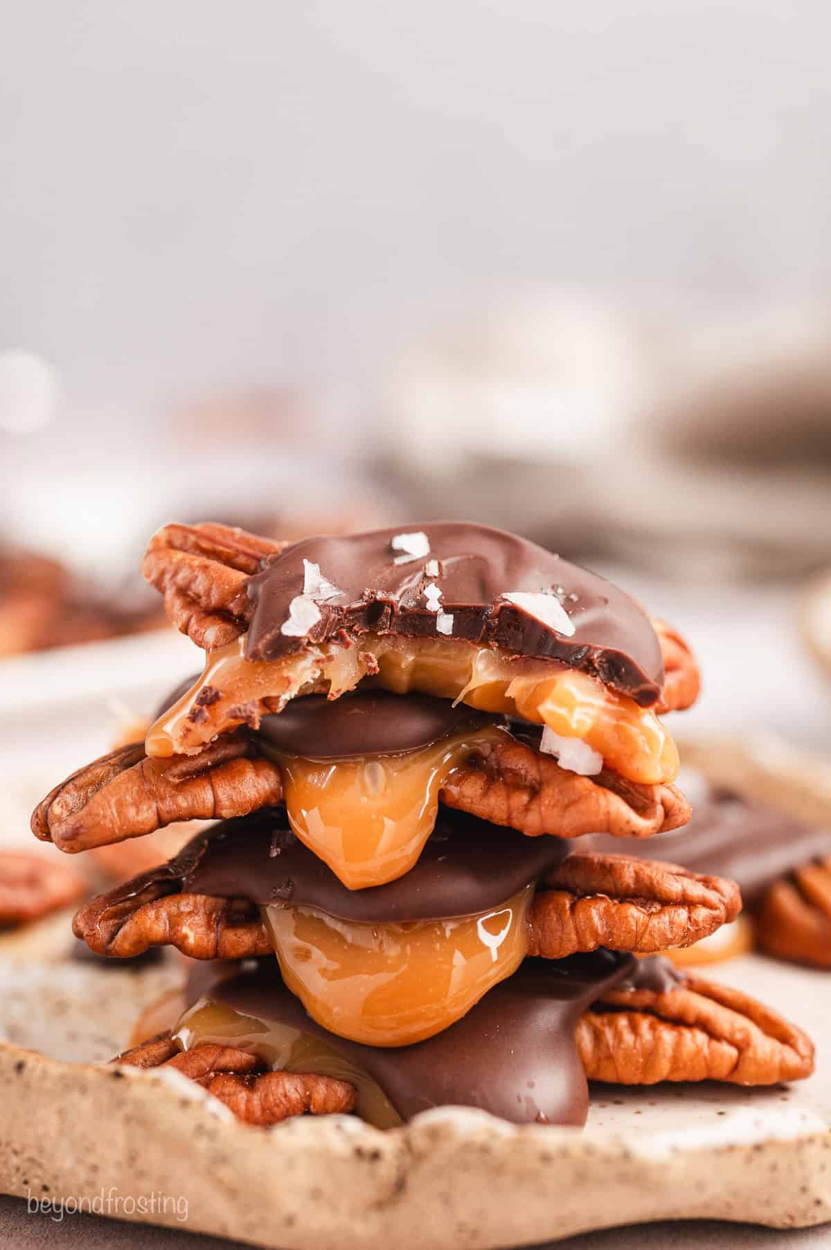 Side view of turtle candies stacked on a wooden cutting board, with a bite missing from the top turtle.