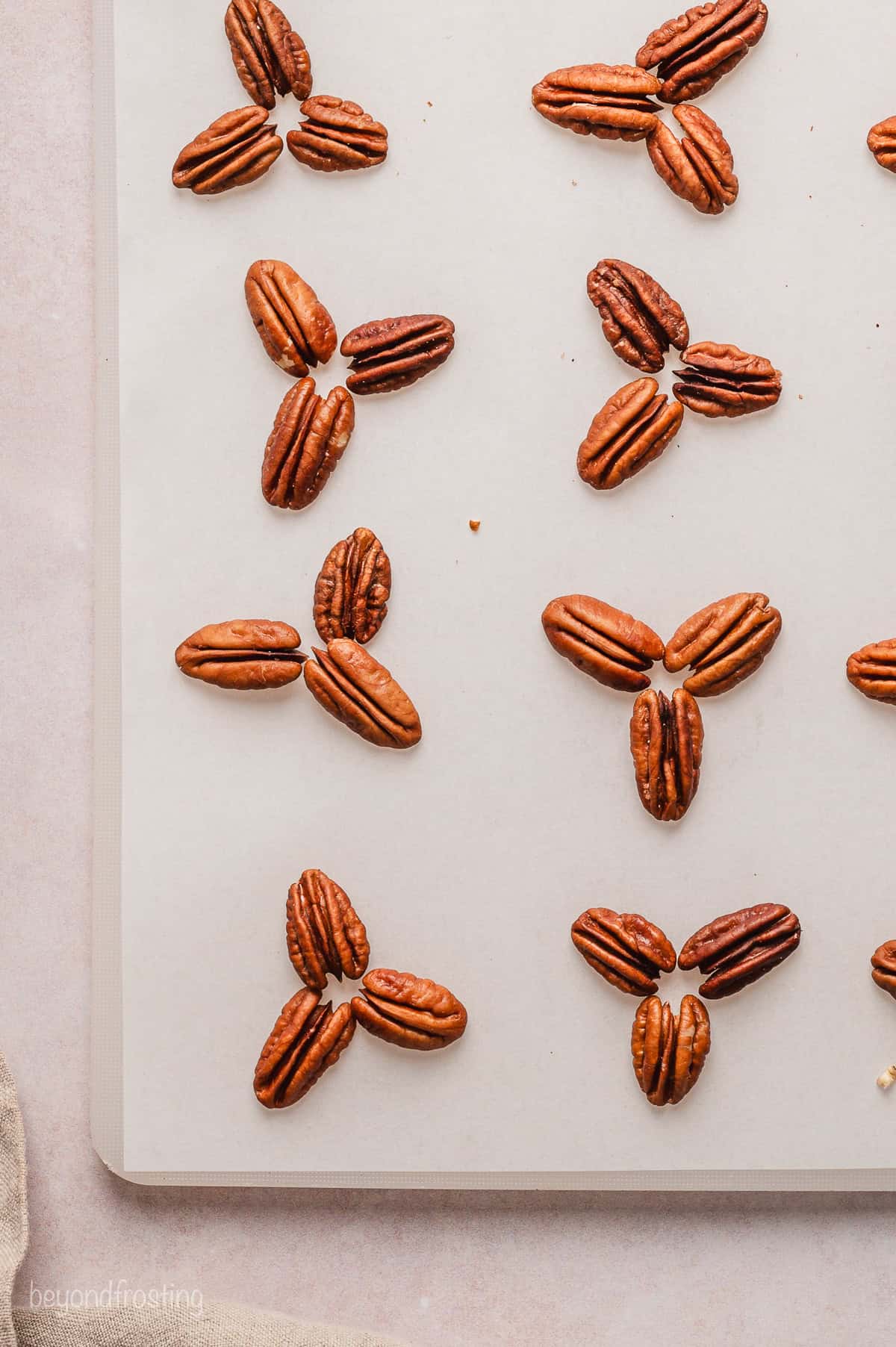 Pecans grouped into threes on a sheet of parchment paper.