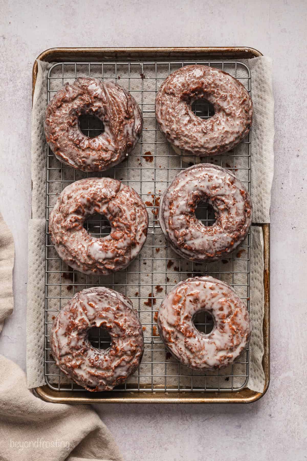 Six glazed chocolate donuts on a wire rack set over a baking sheet.