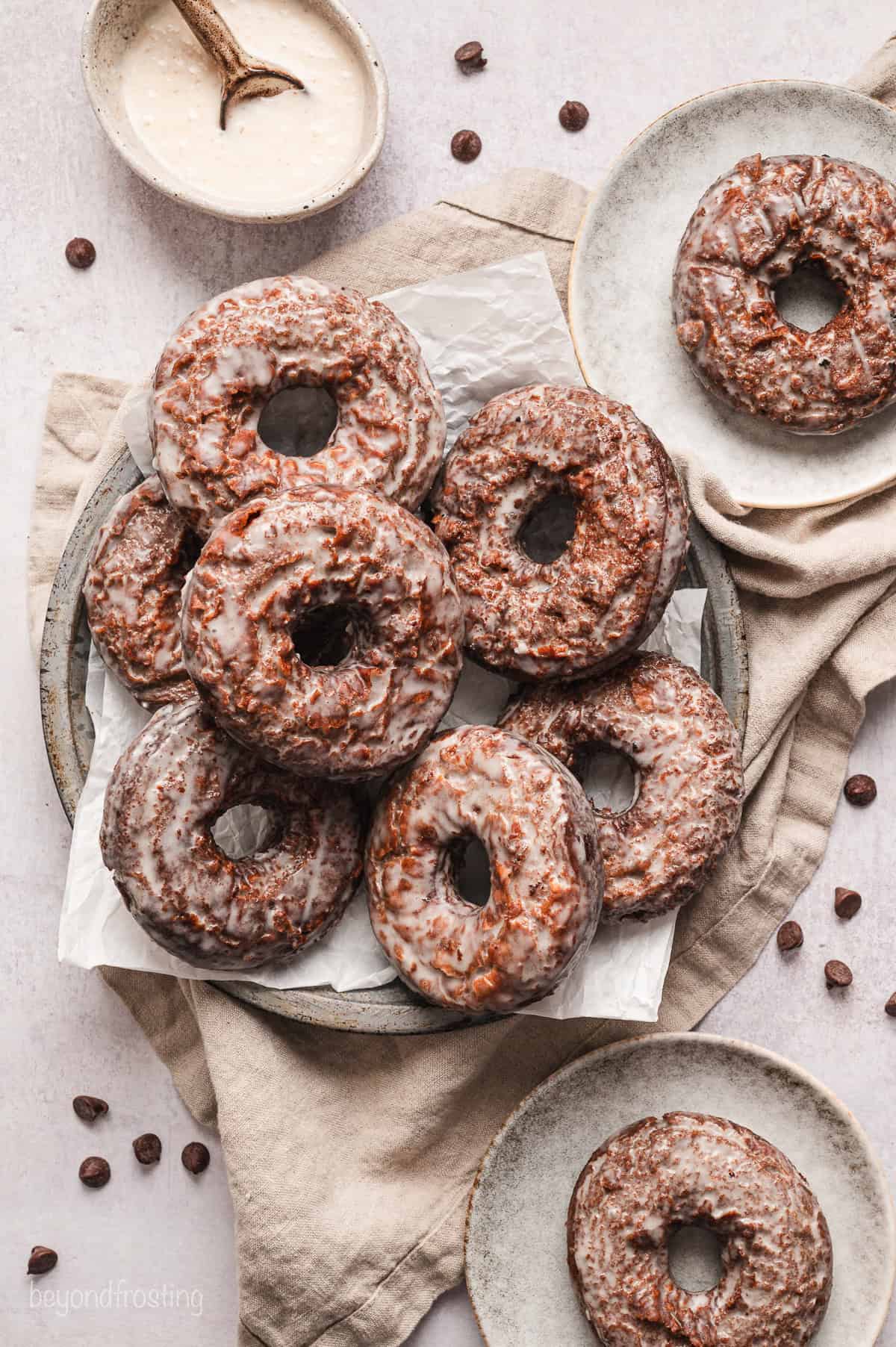 Overhead view of chocolate glazed donuts piled on a plate, next to donuts served on two smaller plates.