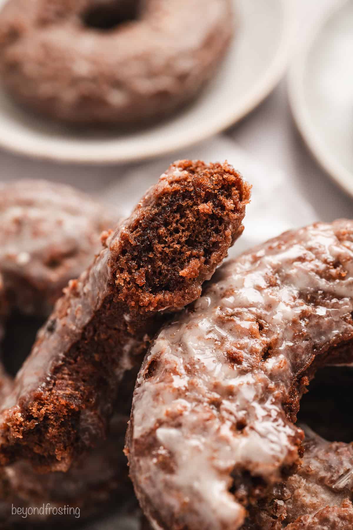 Close up of a chocolate donut broken in half, resting on a pile of whole donuts.