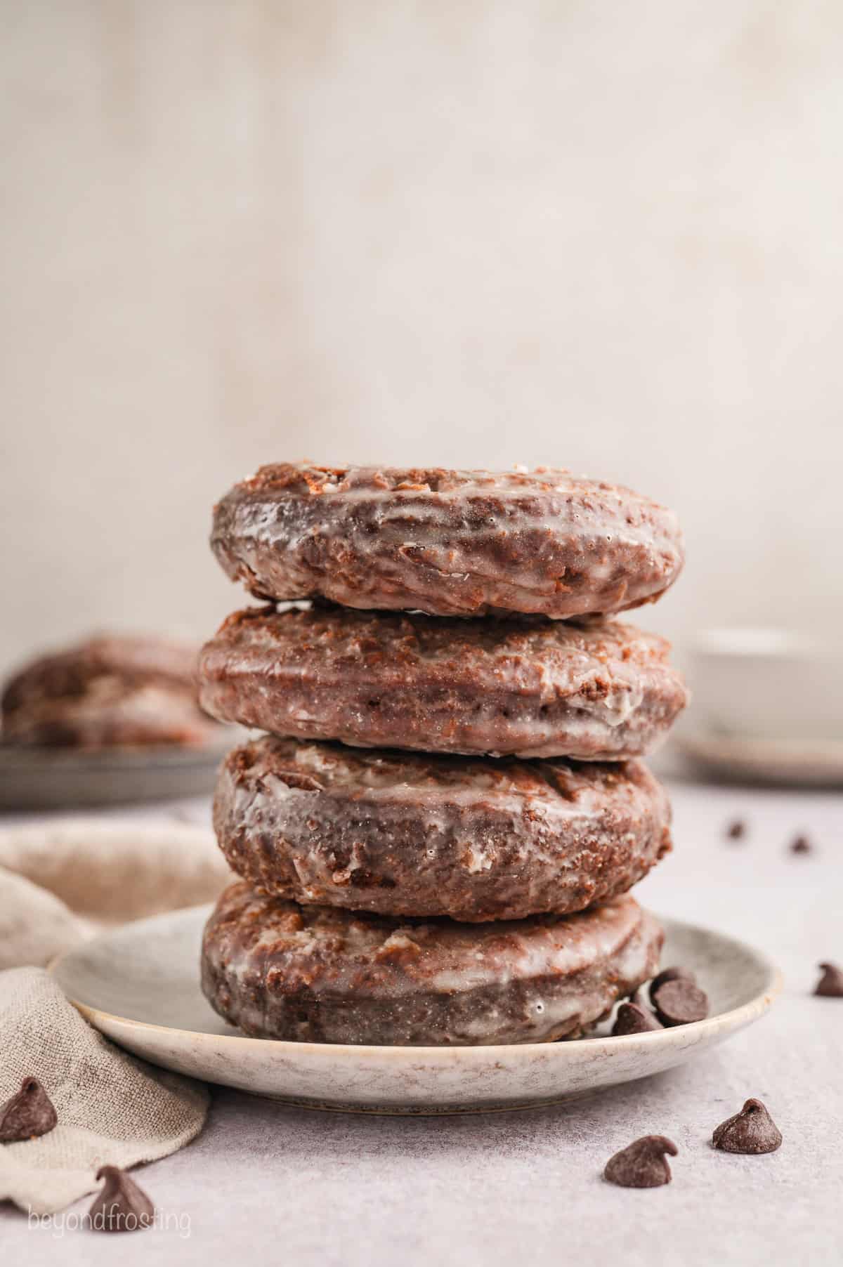 Four chocolate glazed donuts stacked on a white plate.