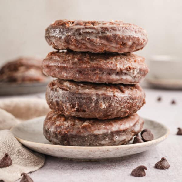 Four chocolate glazed donuts stacked on a white plate.