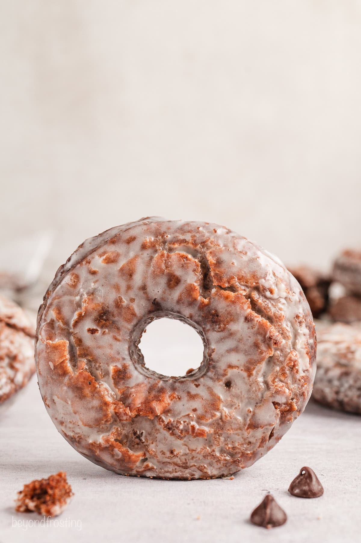 A glazed chocolate donut standing on its side on a white countertop.