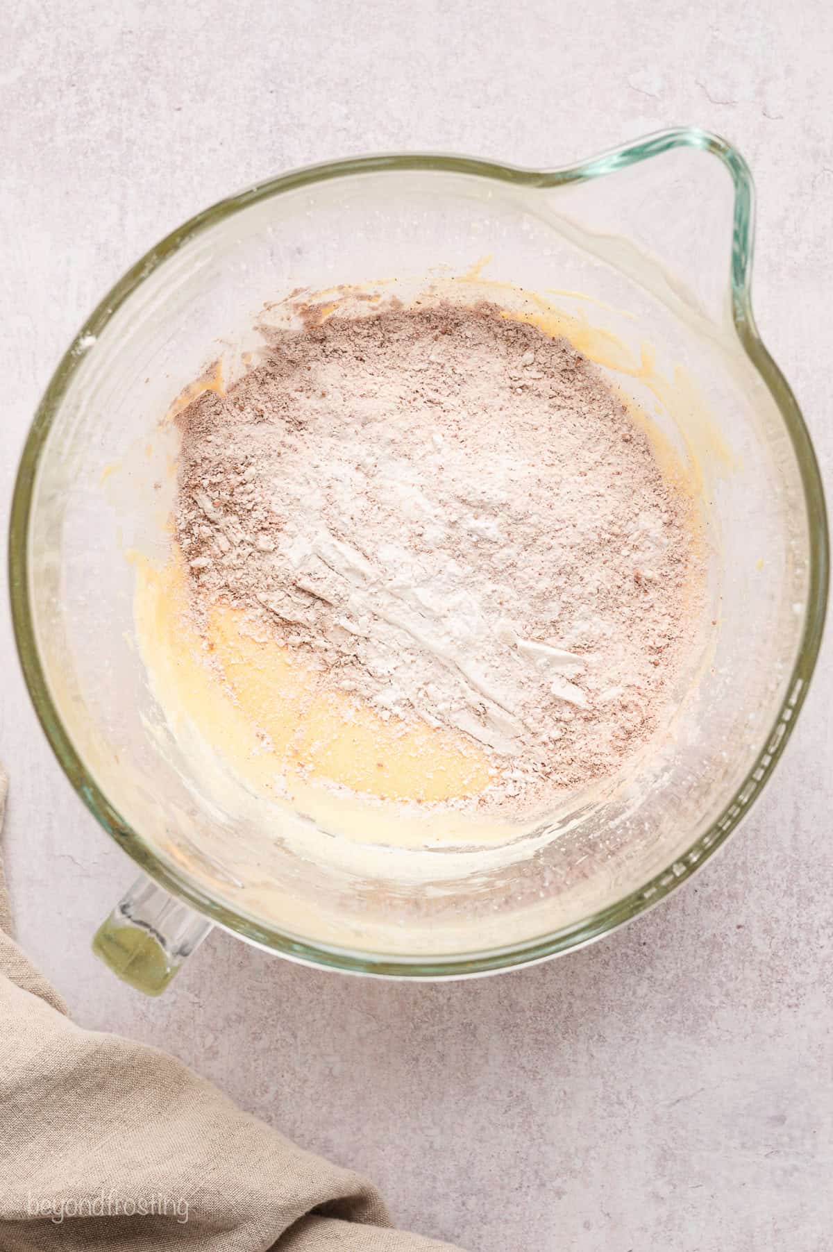 Dry ingredients added to wet donut batter in a mixing bowl.