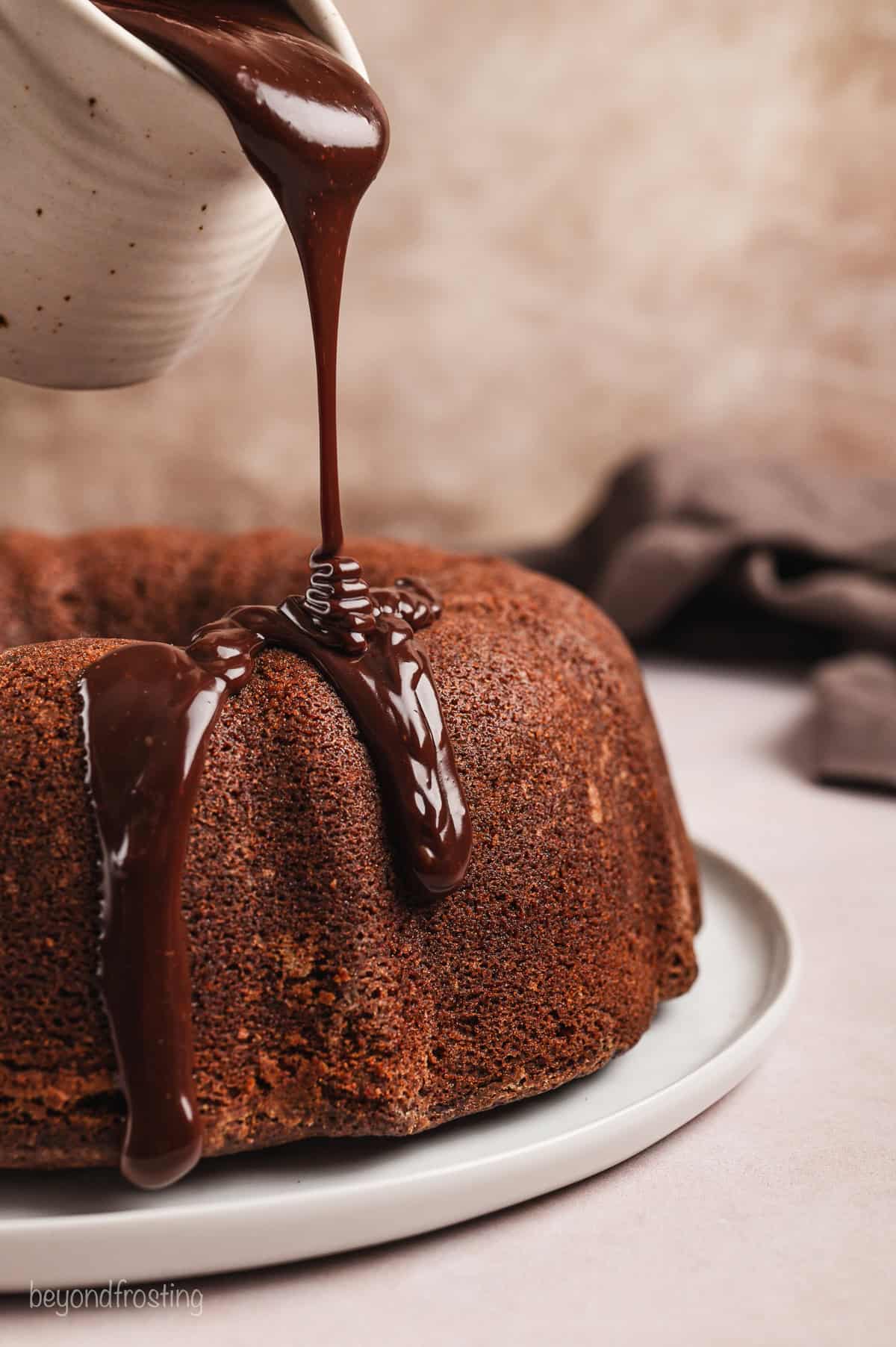 Chocolate ganache being drizzled over top of a chocolate pound cake.