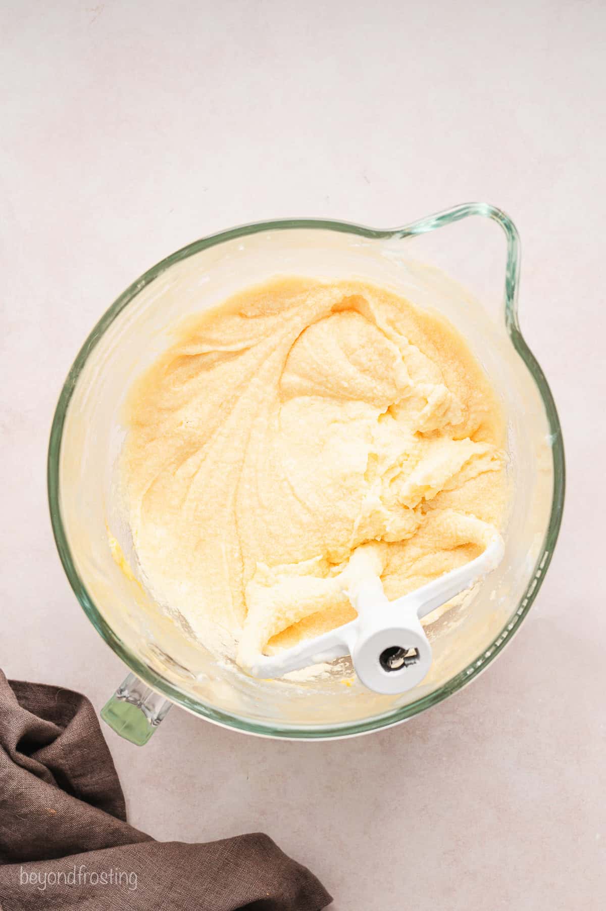 A whisk attachment resting in cake batter in a glass bowl.