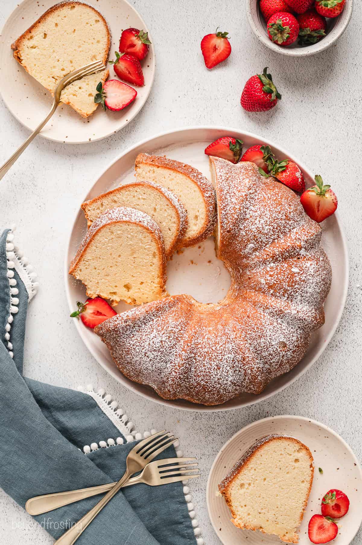 Overhead view of a cream cheese pound cake partially cut into slices on a plate, next to cake slices served on two smaller plates.