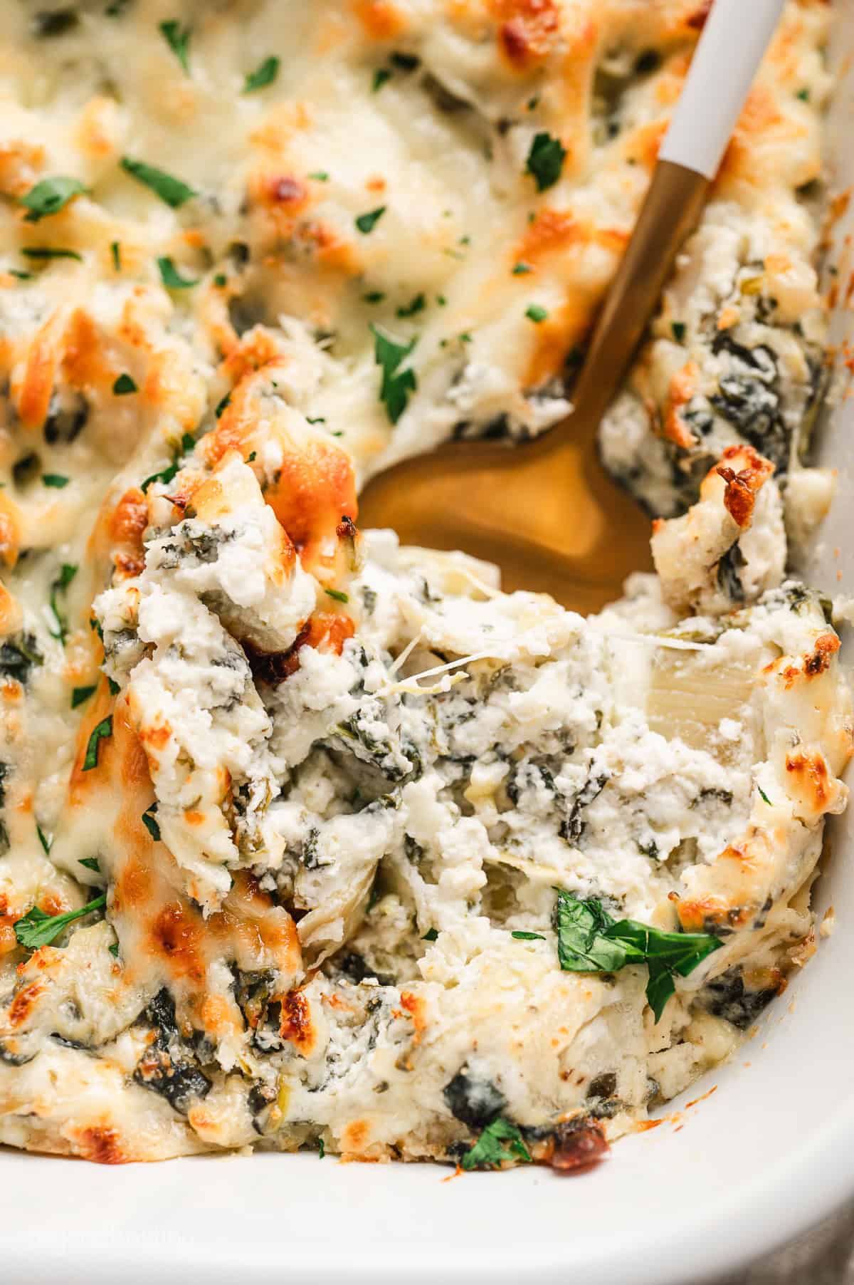 Overhead view of spinach artichoke dip in a large baking dish with a spoon.