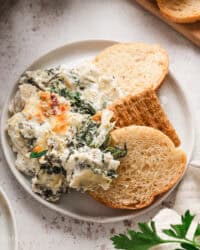 Overhead view of crostini next to spinach artichoke dip on a plate.