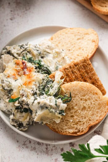 Overhead view of crostini next to spinach artichoke dip on a plate.