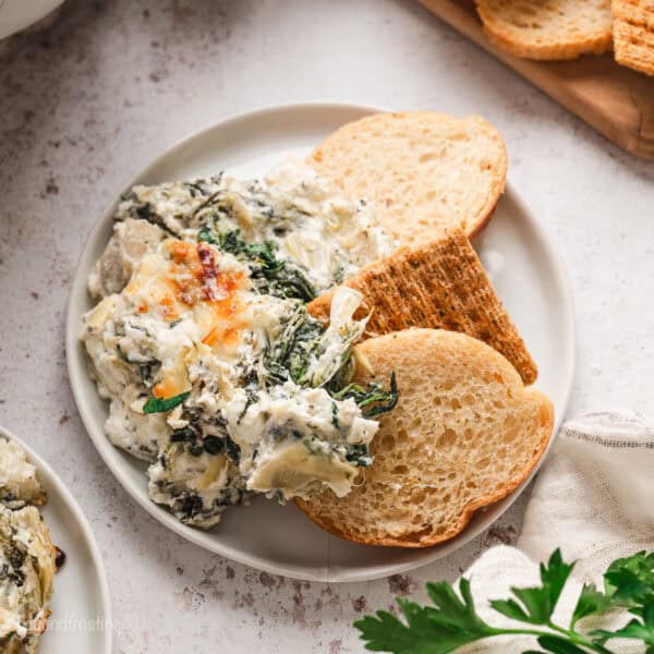 Overhead view of crostini next to spinach artichoke dip on a plate.