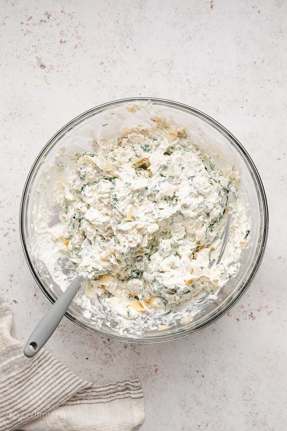 Spinach artichoke dip combined in a glass bowl with a spoon.