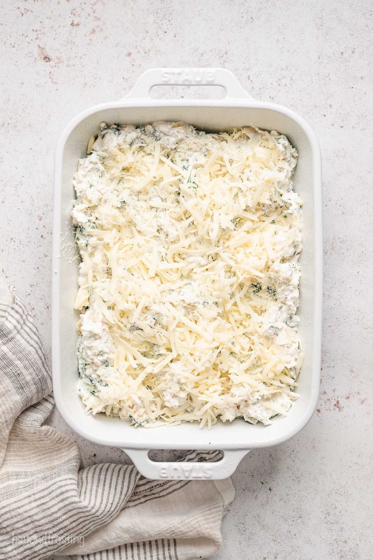 Spinach artichoke dip topped with shredded cheese inside a ceramic baking dish.