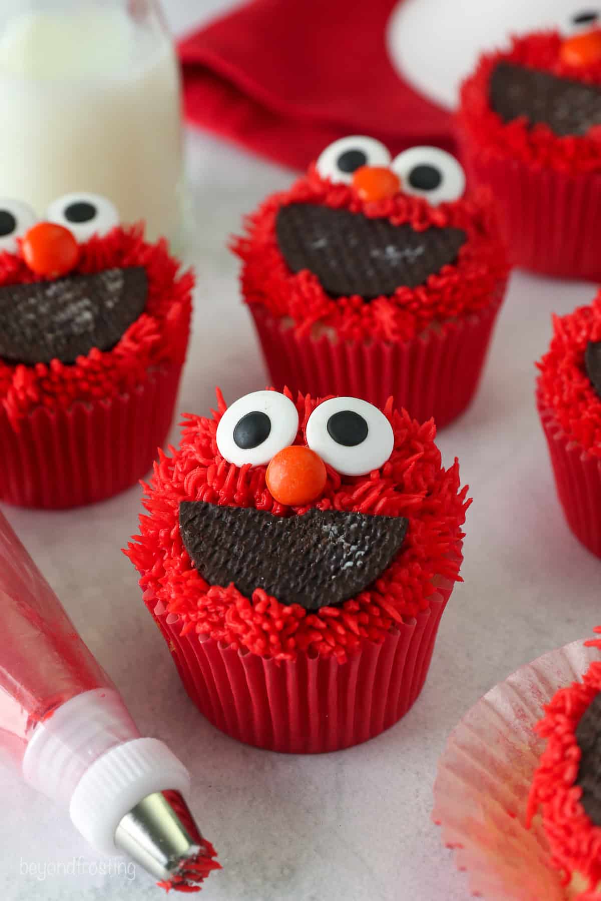 Assorted Elmo cupcakes next to a piping bag fitted with a piping tip on a cuntertop.