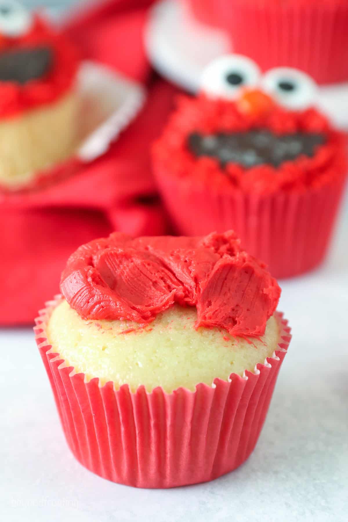 A dollop of red frosting on top of a vanilla cupcake.