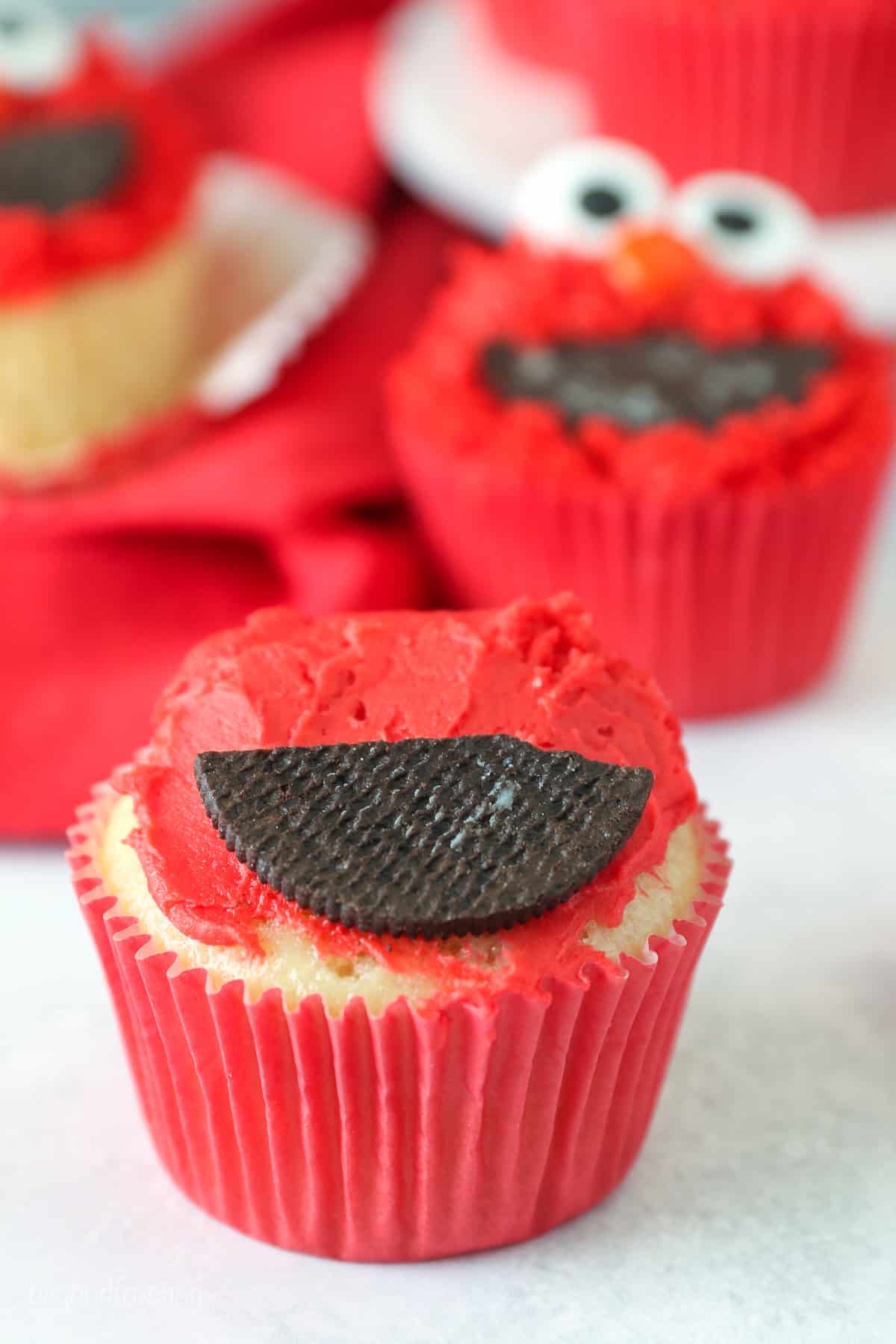 One half of a chocolate cookie placed over a dollop of red frosting on top of a vanilla cupcake.