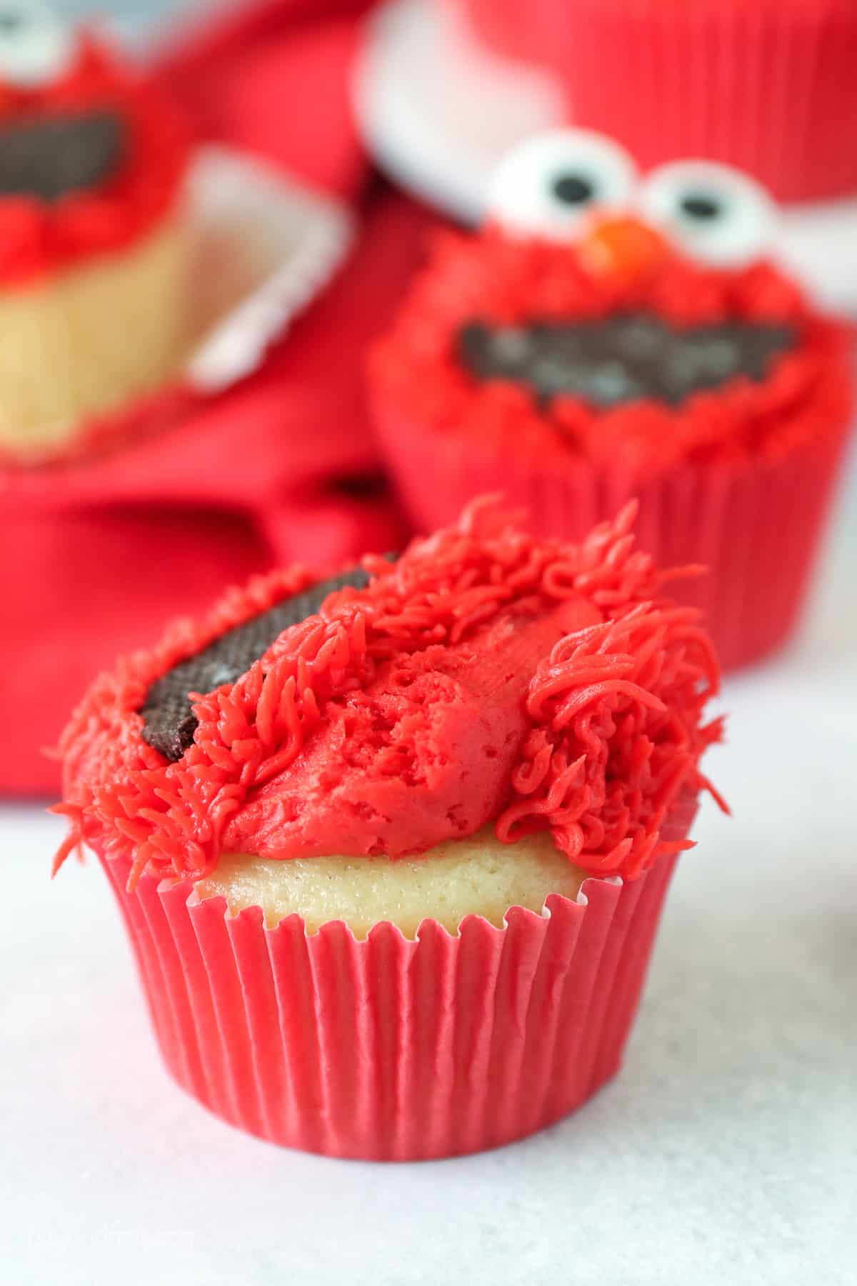 A vanilla cupcake partially decorated with red frosting fur.