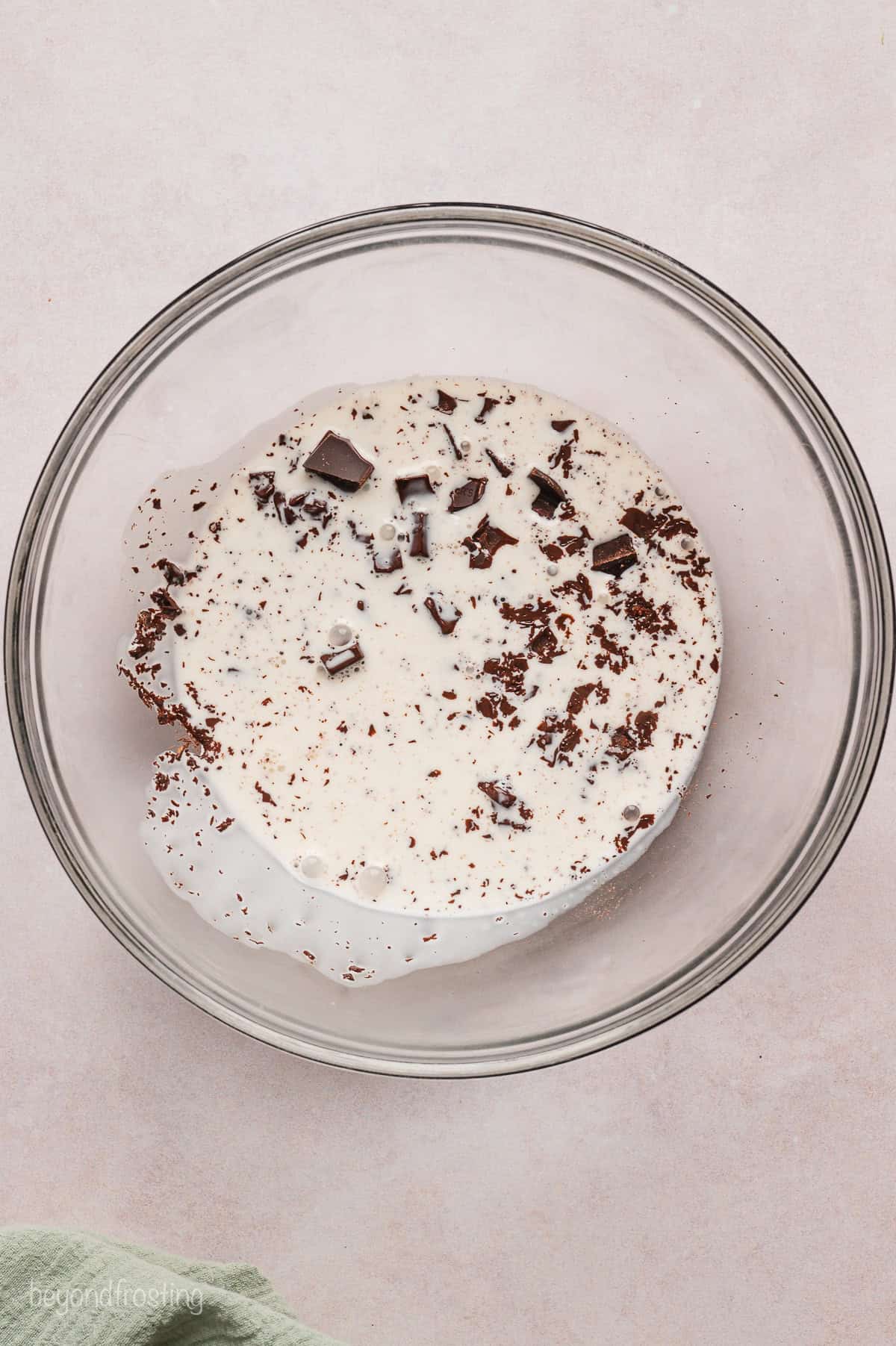 Heavy cream added to chopped chocolate in a glass bowl.