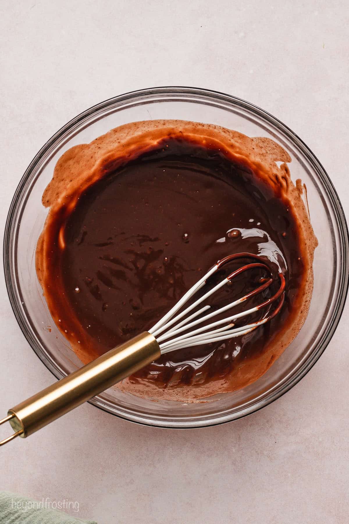 Melted chocolate ganache in a glass bowl with a whisk.