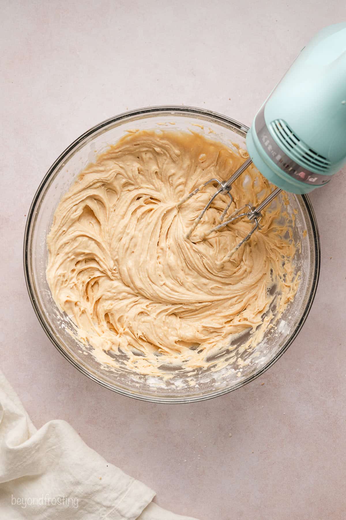 Yellow cake batter combined in a glass bowl with a hand mixer.