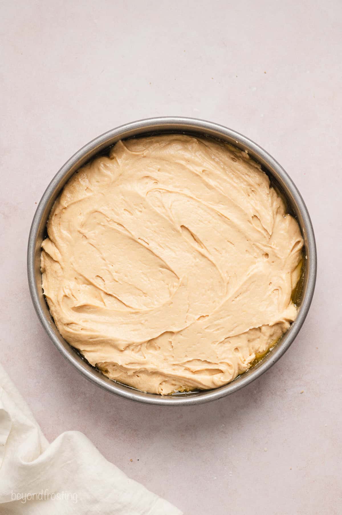 Cake batter spread over the pineapple topping inside a round cake pan.