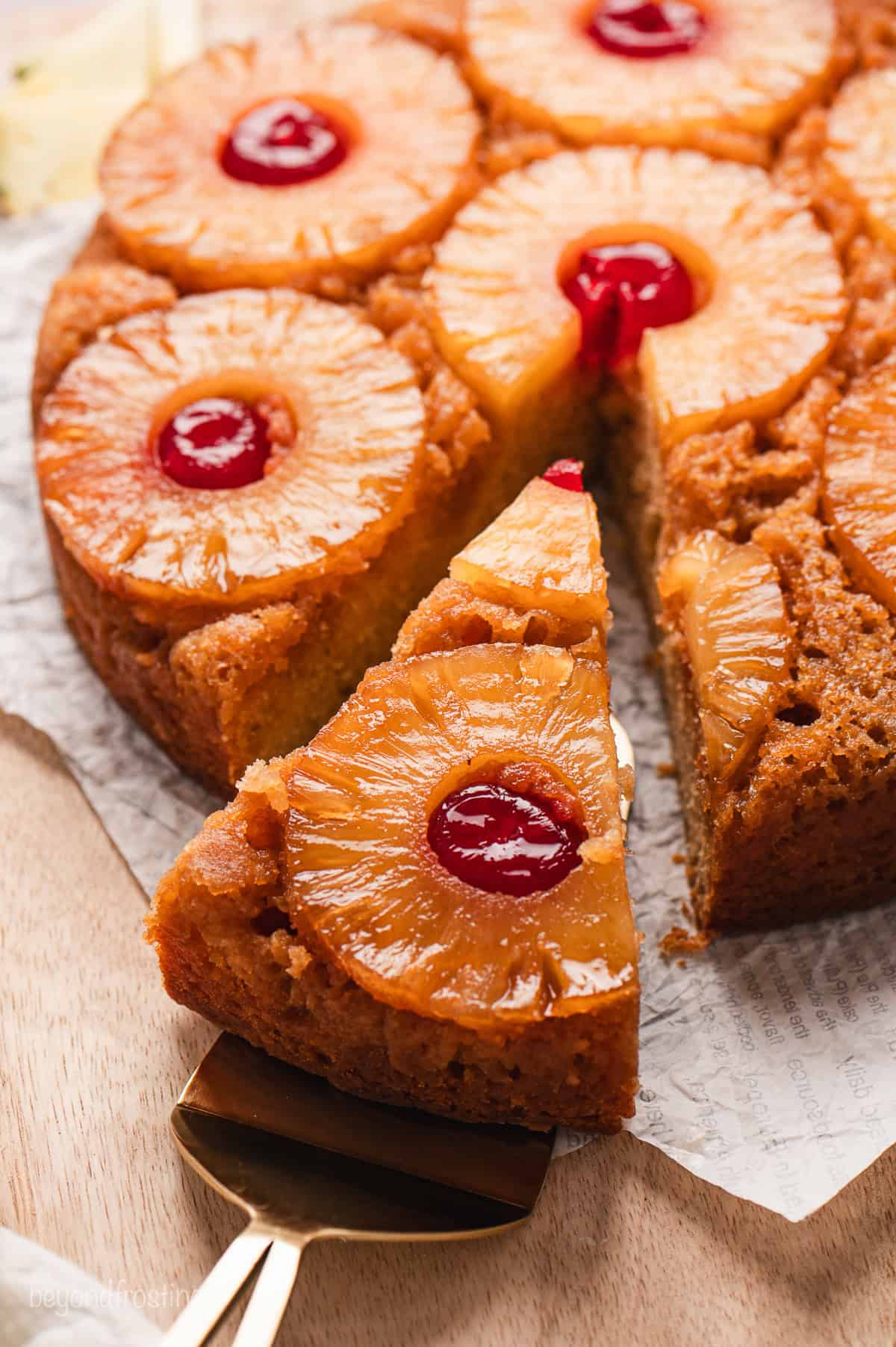 A slice of pineapple upside down cake partially removed from the rest of the cake with a cake server.