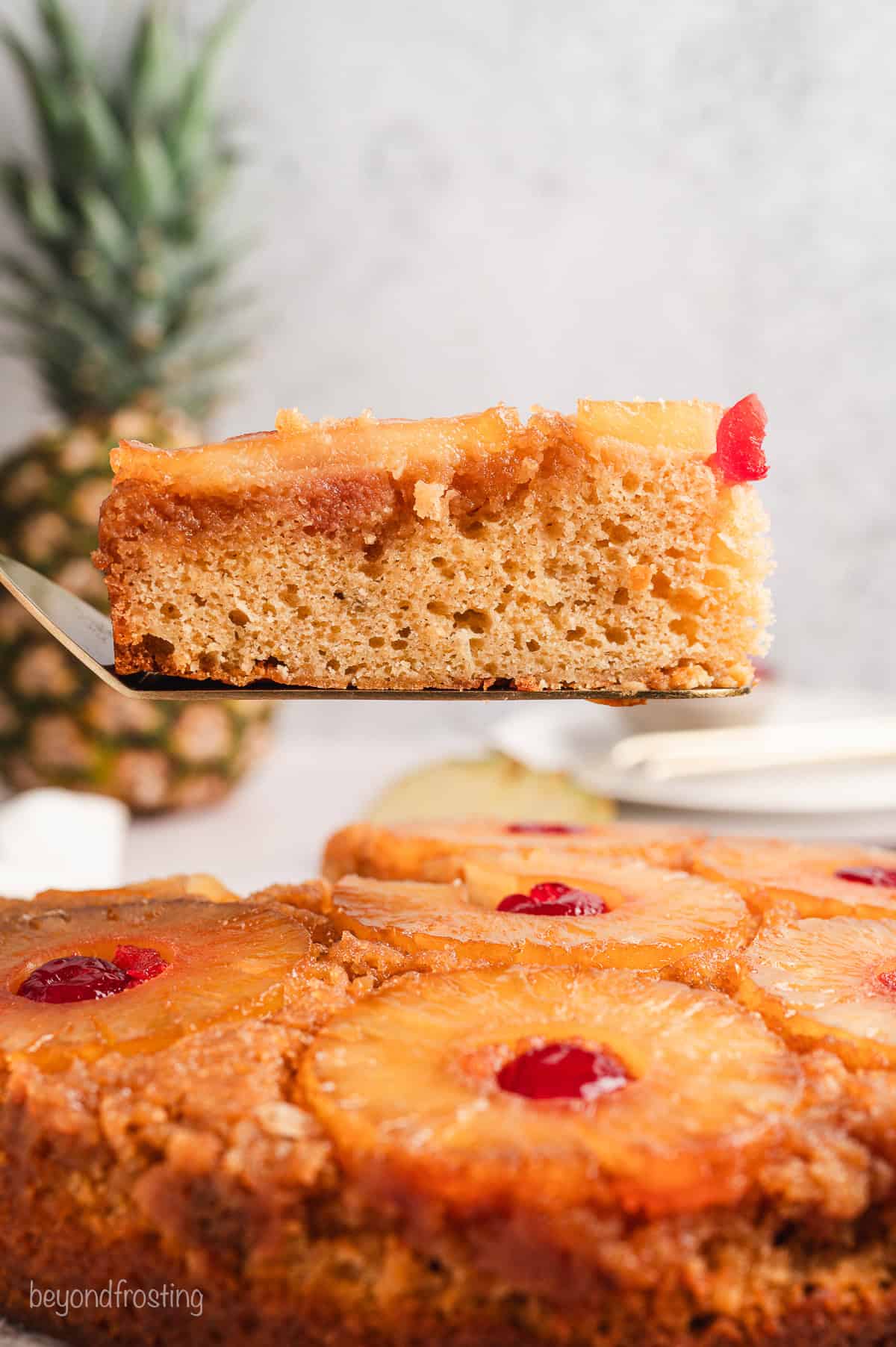 Side view of a slice of pineapple upside down cake being lifted from the rest of the cake with a cake server.