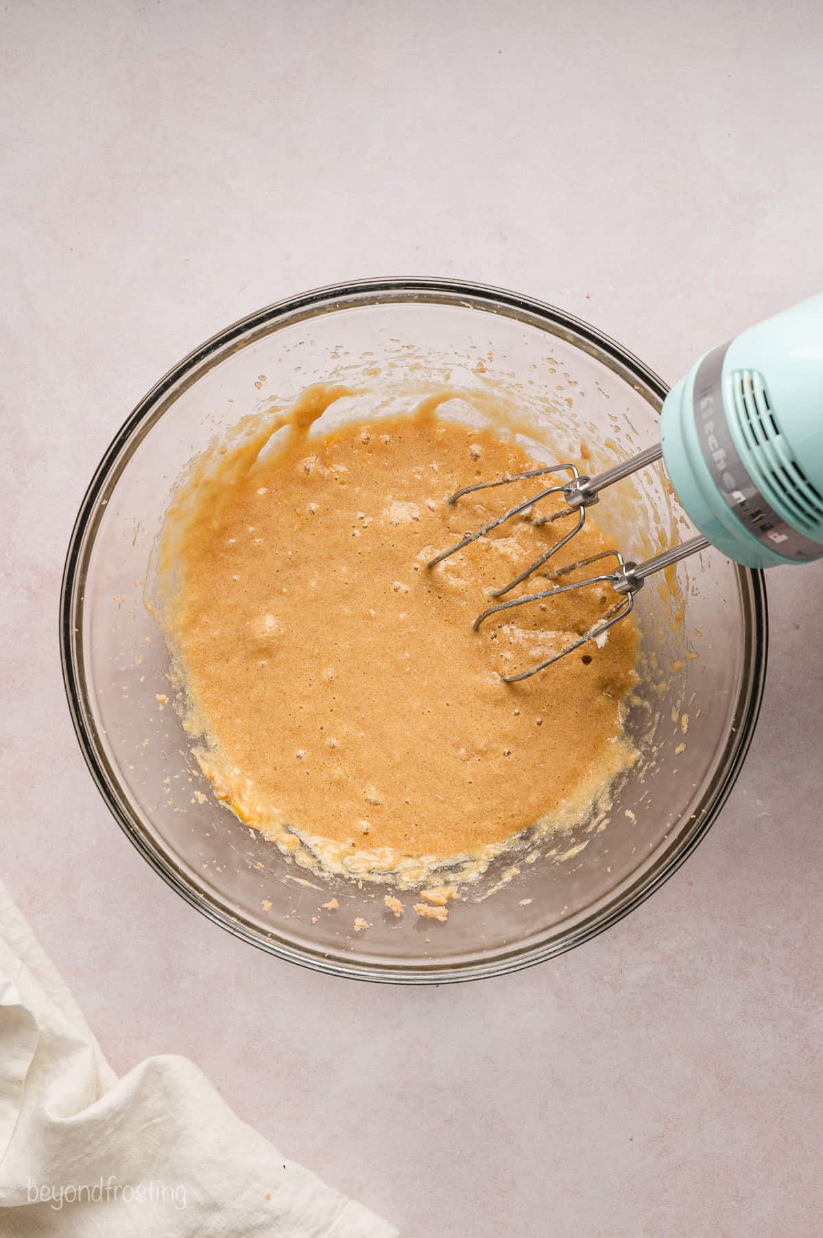 Wet ingredients combined in a glass bowl with a hand mixer.