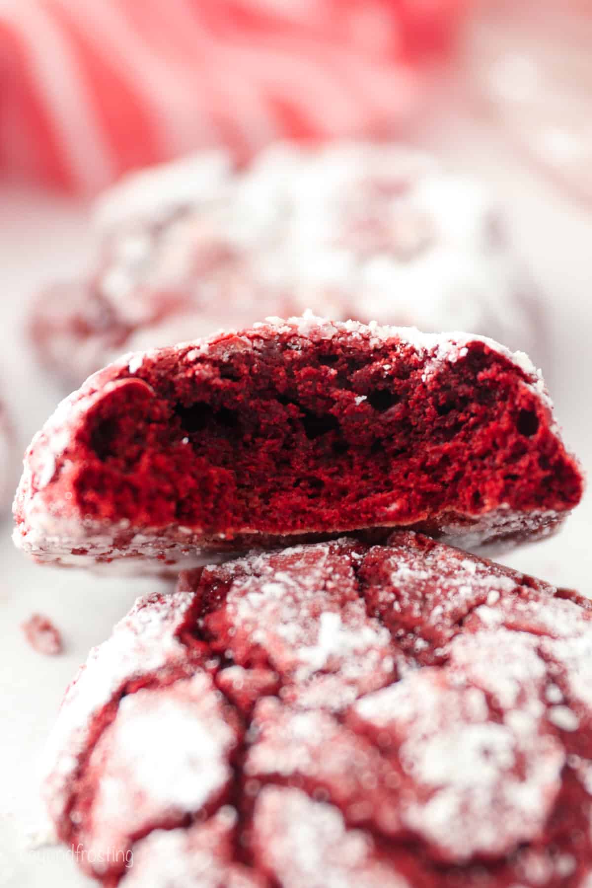 Side view of a red velvet cake mix cookie with a bite missing propped up on top of a another cookie.