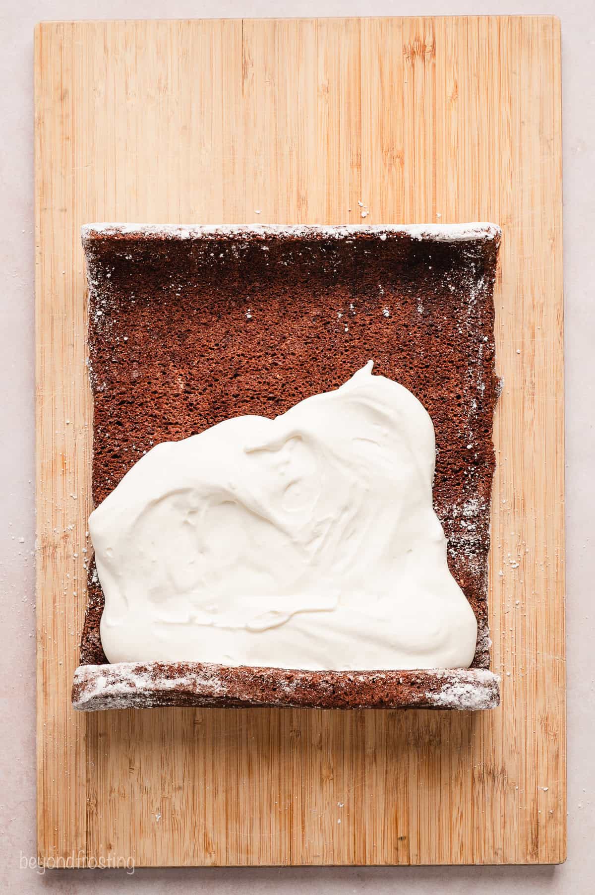 Overhead view of a pre-rolled sheet of chocolate cake partially frosted with cream cheese frosting.