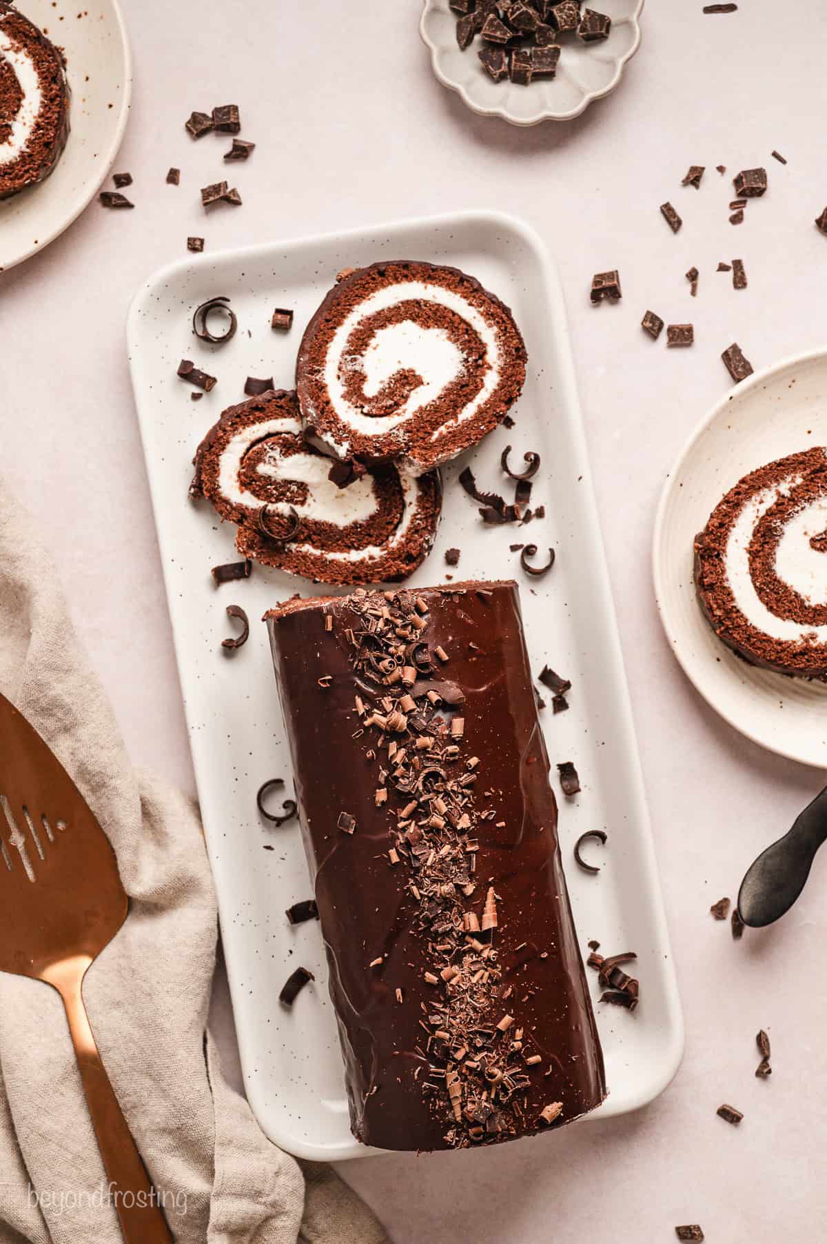 Overhead view of a chocolate cake roll topped with chocolate shavings, with two slices cut from the end on a long platter.