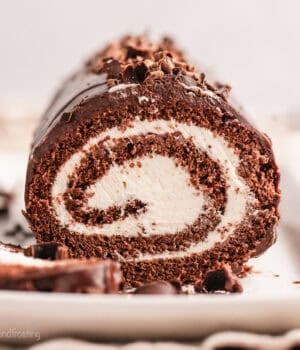 Front view of a chocolate cake roll topped with chocolate shavings, with a slice cut from the end.