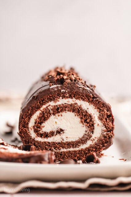 Front view of a chocolate cake roll topped with chocolate shavings, with a slice cut from the end.