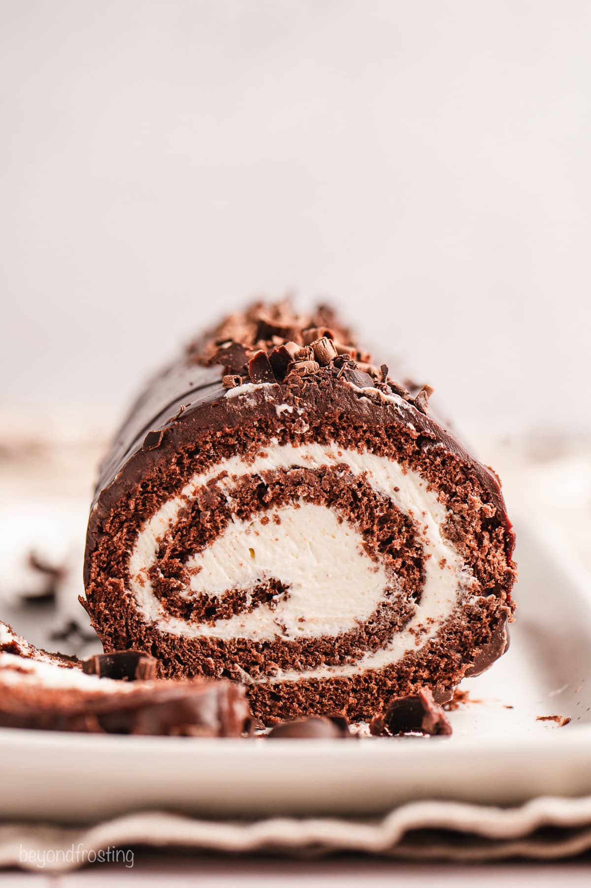 A Swiss cake roll for a crowd, this chocolate cake roll is a soft chocolate sponge cake rolled with cream cheese filling, covered in ganache. Front view of a chocolate cake roll topped with chocolate shavings, with a slice cut from the end.